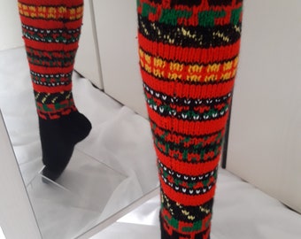 May include: A pair of knee-high knitted socks featuring a vibrant pattern of red, black, yellow, and green horizontal stripes. The socks have a solid black cuff at the top and a solid black foot section, with a detailed geometric knit design throughout.