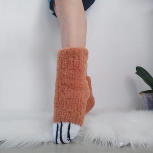 May include: A pair of fuzzy orange socks with white and navy blue stripes at the top. The socks are made of a soft, plush material.