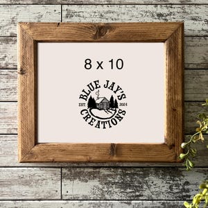 May include: A rectangular wooden frame with a light-colored insert featuring the black text 8 x 10 and a circular logo with a cabin, trees, and the text Blue Jay's Creations Est. 2024. The frame has a natural wood grain finish and mitered corners.
