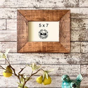 May include: A rustic wooden picture frame with a 5x7 inch opening. The frame is stained a dark brown color and has a distressed finish. The frame is sitting on a white wooden background. The text "Blue Jays Creations" is visible in the frame.
