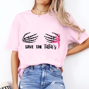 May include: Pink t-shirt with a black skeleton hand graphic and a pink ribbon. The text "Save the Tata's" is printed below the graphic.
