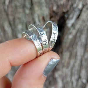 Könnte beinhalten: Drei silberne Ringe mit einem Mond- und Sternendesign. Die Ringe sind übereinander gestapelt.