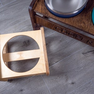 May include: Two wooden elevated pet food bowls, one with a teal bowl and the other with a blue bowl. The bowls are on a wooden stand with the name "COOPER" engraved on the front.