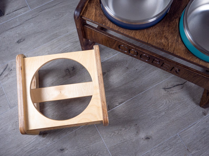 May include: Two wooden elevated pet food bowls, one with a teal bowl and the other with a blue bowl. The bowls are on a wooden stand with the name "COOPER" engraved on the front.