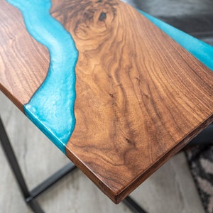 May include: A wooden table top with a blue epoxy resin river design. The table top is made of walnut wood and has a natural wood finish. The epoxy resin is clear and has a smooth, glossy finish.