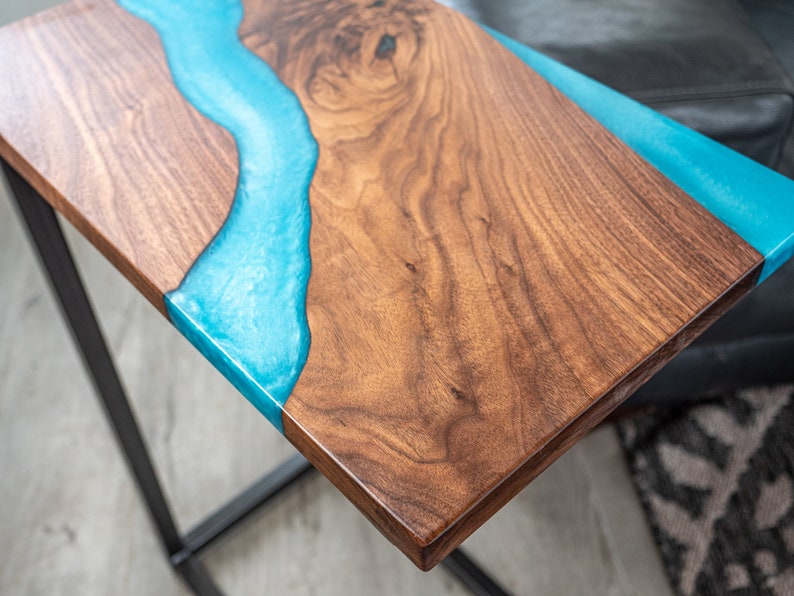 May include: A wooden table top with a blue epoxy resin river design. The table top is made of walnut wood and has a natural wood finish. The epoxy resin is clear and has a smooth, glossy finish.
