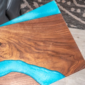 May include: A wooden table top with a blue epoxy river running through it. The wood has a natural grain pattern.