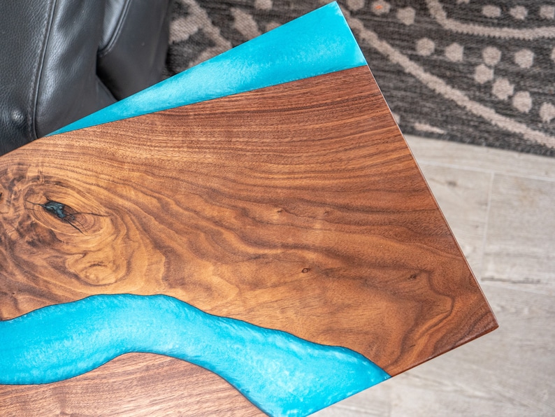 May include: A wooden table top with a blue epoxy river running through it. The wood has a natural grain pattern.