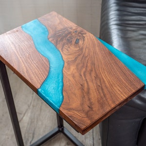 May include: A wooden side table with a blue resin river design. The table has a black metal frame.