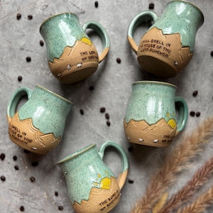 May include: Five ceramic mugs with a speckled light green glaze on the upper half and a textured tan base. Each mug features a mountain landscape, a yellow sun, small sheep, and the text "The Lord is my shepherd" or "I will dwell in the house of the Lord forever."
