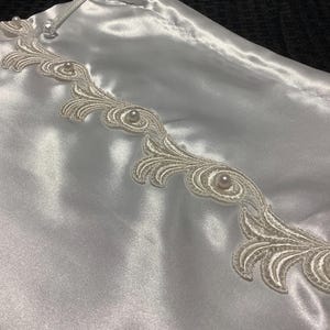 May include: White satin drawstring bag with a delicate white lace trim and pearl embellishments.