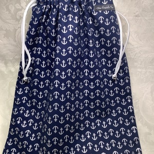 May include: A navy blue drawstring bag with a white anchor pattern. The bag has a white drawstring and a black label that says "Chic Travels Too".