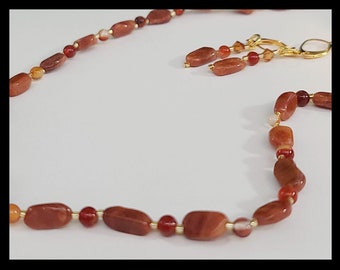 May include: A necklace and earrings set made with brown, orange, and red gemstone beads. The necklace is made with a gold chain and the earrings are made with gold hoops.