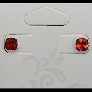 May include: A pair of red gemstone earrings on a white card with a cut-out shape.