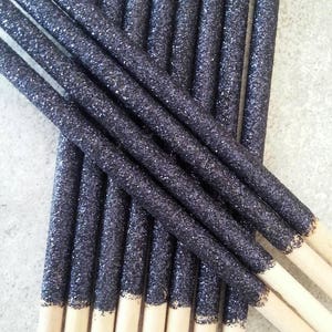 K&ouml;nnte beinhalten: Ein B&uuml;ndel schwarzer, mit Glitzer &uuml;berzogener Holzspie&szlig;e. Die Spie&szlig;e sind etwa 15 cm lang und haben eine nat&uuml;rliche Holzoptik auf der unteren H&auml;lfte.