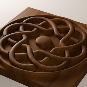 Puede incluir: Una placa de madera cuadrada con un dise&ntilde;o circular tallado que presenta un patr&oacute;n de nudos entrelazados en relieve. El centro de la pieza muestra un disco de madera liso y circular rodeado por un relieve continuo, tejido y redondeado.