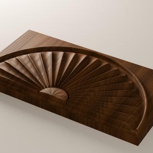 May include: A rectangular dark brown wooden block featuring a carved semi-circular fan pattern. The design consists of multiple radiating grooves that originate from a central point, creating a textured, dimensional surface on the wood.