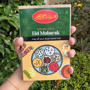 May include: A greeting card with the text "Eid Mubarak" and a colorful illustration of various dishes. The card has a green and tan color scheme, with Arabic script at the top. The phrase "may all your duas come true" is also included.