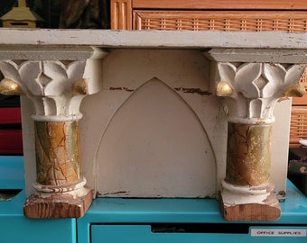 May include: A white wooden shelf with two decorative columns on either side. The columns are painted with gold and green accents. The shelf has a pointed arch in the center.