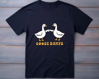 May include: A navy blue t-shirt featuring a graphic of two white geese facing each other and holding hands. The text "GOOSE BUMPS" is printed in yellow below the geese.
