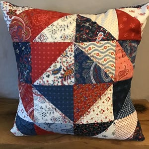 May include: A red, white, and blue patchwork pillow with a geometric pattern. The pillow is made of different fabrics with floral and paisley designs.