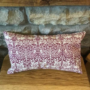 Peut inclure: Un coussin rectangulaire avec un fond bordeaux et un motif floral blanc. Le coussin est posé sur une surface en bois.