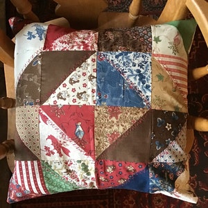 May include: A patchwork cushion featuring a mix of floral and geometric patterns in shades of red, blue, brown, and white.