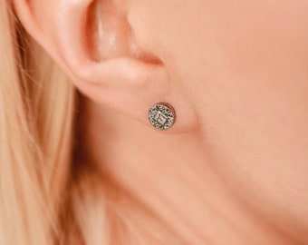 May include: A close-up of a person's ear with a small, silver earring featuring a textured, circular design.