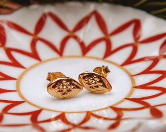 May include: A pair of gold-toned earrings with a geometric design, displayed on a white saucer with a red and gold pattern.