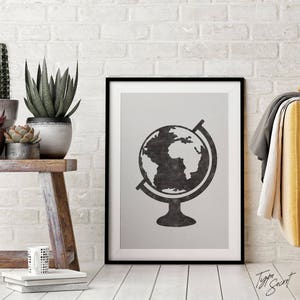 May include: Black and white print of a globe on a stand in a black frame. The globe is a stylized illustration of the Earth with continents and oceans.
