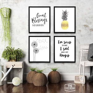 May include: Four black framed prints with white backgrounds and black text. The top left print says "Count Blessings Not Calories". The top right print features a gold pineapple on a white background. The bottom left print features a black and white illustration of two dandelions with seeds blowing in the wind. The bottom right print says "I'm sorry for what I said when I was Hangry".