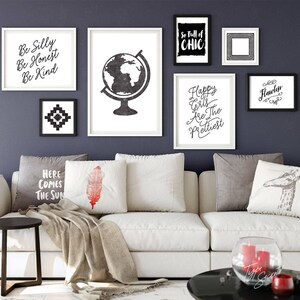 May include: A white couch with gray and white pillows, a throw blanket, and a small round table with a vase of flowers. The wall behind the couch is painted a dark gray and decorated with black and white framed prints with inspirational quotes, including "Be Silly, Be Honest, Be Kind", "So Full of Chic", "Happy Girls Are The Prettiest", "Flawless", and a globe.