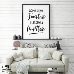 Puede incluir: Impresi&oacute;n tipogr&aacute;fica en blanco y negro con el texto "Once you become fearless life becomes limitless". La impresi&oacute;n est&aacute; enmarcada en un marco negro y est&aacute; colgada en una pared de madera blanca sobre un sof&aacute; blanco con almohadas y una manta.