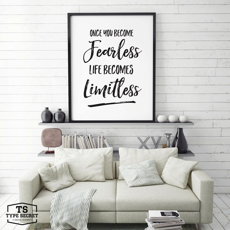 Puede incluir: Impresi&oacute;n tipogr&aacute;fica en blanco y negro con el texto "Once you become fearless life becomes limitless". La impresi&oacute;n est&aacute; enmarcada en un marco negro y est&aacute; colgada en una pared de madera blanca sobre un sof&aacute; blanco con almohadas y una manta.
