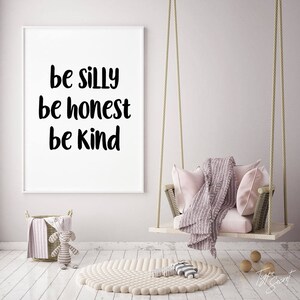 K&ouml;nnte beinhalten: Ein wei&szlig;er gerahmter Druck mit dem Text "be silly be honest be kind" h&auml;ngt an einer hellrosa Wand. Ein rosa-wei&szlig;er Schaukelstuhl h&auml;ngt vor dem Druck. Ein wei&szlig;er Teppich mit strukturierter Oberfl&auml;che liegt auf dem Boden.