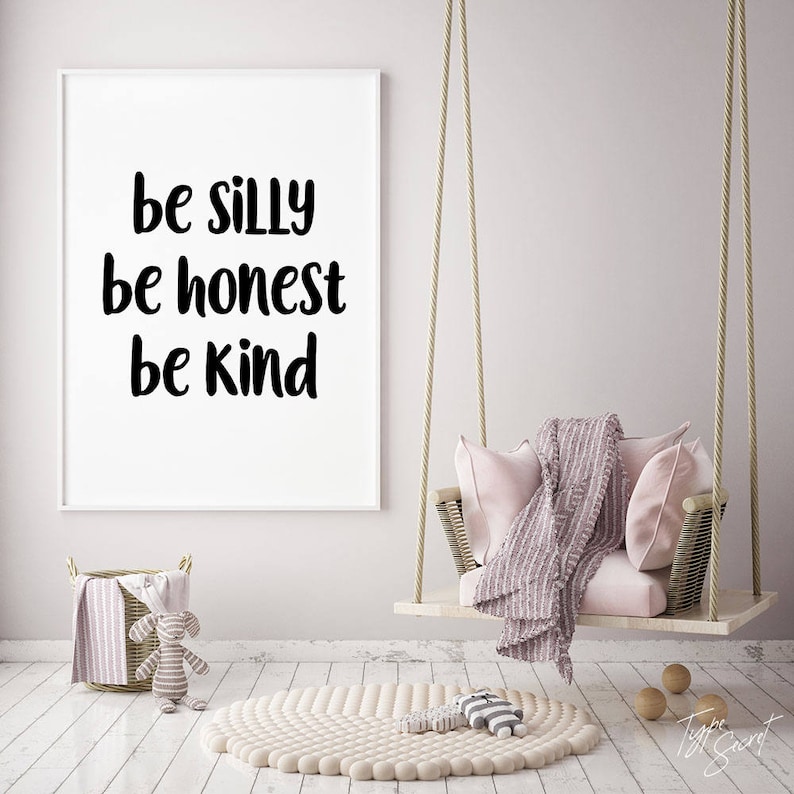 K&ouml;nnte beinhalten: Ein wei&szlig;er gerahmter Druck mit dem Text "be silly be honest be kind" h&auml;ngt an einer hellrosa Wand. Ein rosa-wei&szlig;er Schaukelstuhl h&auml;ngt vor dem Druck. Ein wei&szlig;er Teppich mit strukturierter Oberfl&auml;che liegt auf dem Boden.