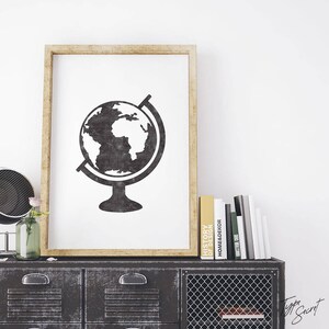 May include: A black and white illustration of a globe on a stand, printed on a white background and framed in a light wood frame. The print is displayed on a black metal cabinet with a wire mesh door.