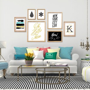 May include: A white couch with colorful pillows and a black and white striped rug. The wall behind the couch is decorated with framed artwork, including a black and white print with the text "Oh Hello There", a black and white print with the text "Meow", a black and white print with the text "New York City Girl", and a black and white print with the text "K".