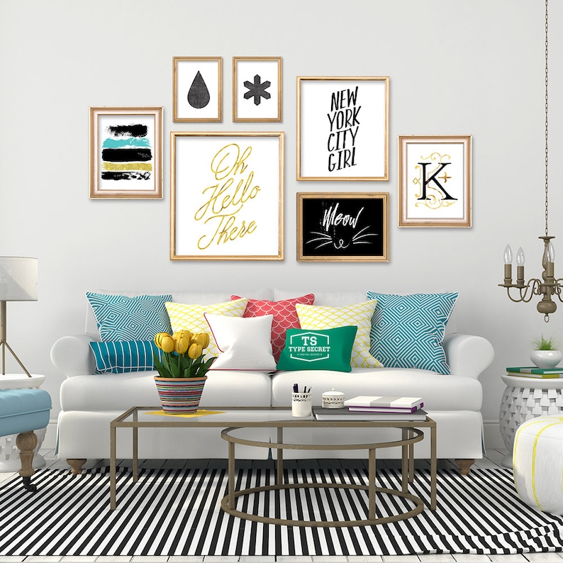 May include: A white couch with colorful pillows and a black and white striped rug. The wall behind the couch is decorated with framed artwork, including a black and white print with the text "Oh Hello There", a black and white print with the text "Meow", a black and white print with the text "New York City Girl", and a black and white print with the text "K".