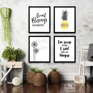 May include: Four black framed prints with white backgrounds and black text. The top left print says "Count Blessings Not Calories". The top right print features a gold pineapple on a white background. The bottom left print features a black and white illustration of two dandelions with seeds blowing in the wind. The bottom right print says "I'm sorry for what I said when I was Hangry".