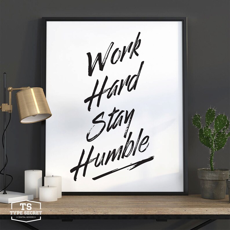 Puede incluir: Impresi&oacute;n de una cita motivacional en blanco y negro en un marco negro. La cita dice "Work Hard Stay Humble" con una flecha negra apuntando hacia la derecha.