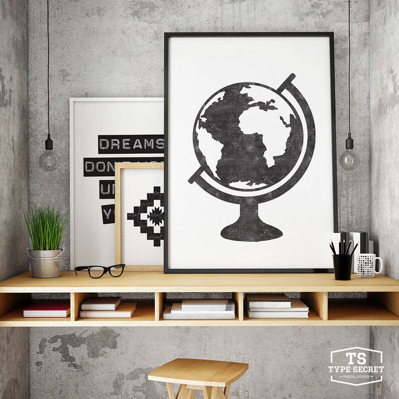 May include: A wooden shelf unit with three shelves, each containing books. The shelf is mounted on a gray concrete wall. There are two black framed prints above the shelf, one with a globe and the other with the text "DREAMS DON'T" and a geometric pattern.