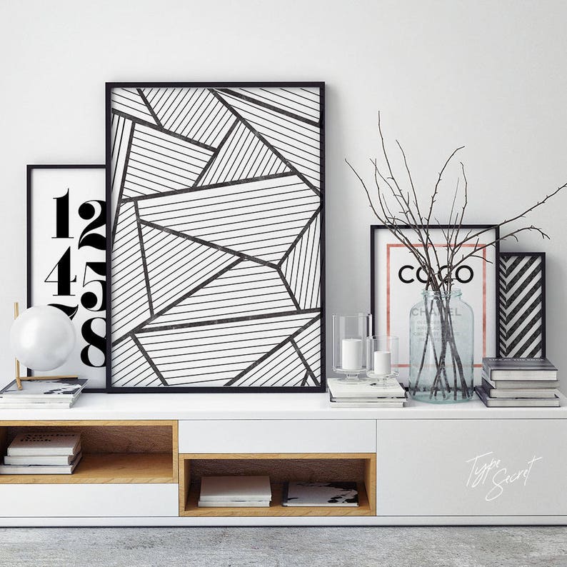 May include: A white media console with a wood-toned shelf and two drawers. The console is decorated with three framed prints, two candles, a vase with branches, and books. The prints feature black and white geometric designs and the text "Coco".
