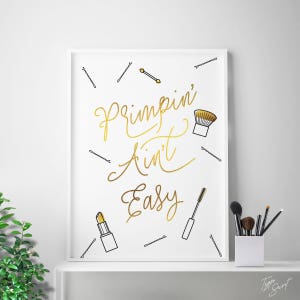 May include: A white framed print with gold lettering that reads "Primpin' Ain't Easy". The print is surrounded by black and white illustrations of hair clips, makeup brushes, lipstick, and mascara.