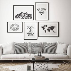 May include: A white couch with black and white striped pillows in front of a white wall with black framed prints. The prints feature a mountain range, a world map, a quote about adventure, and a diamond shape with the word "Adventure" inside.
