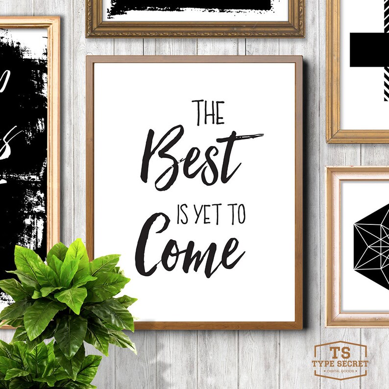 Puede incluir: Impresi&oacute;n tipogr&aacute;fica en blanco y negro con el texto "The Best is Yet to Come" en un estilo de caligraf&iacute;a moderno. La impresi&oacute;n est&aacute; enmarcada en un marco de madera marr&oacute;n claro y est&aacute; colgada en una pared blanca.