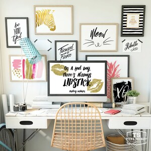 Puede incluir: Un escritorio blanco con un monitor de computadora que muestra una cita sobre el l&aacute;piz labial. La cita dice "On a bad day, there's always lipstick." de Audrey Hepburn. El escritorio tiene una silla blanca, una c&aacute;mara, una pi&ntilde;a y otra decoraci&oacute;n.