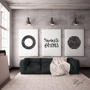 Puede incluir: Tres impresiones de arte minimalistas en blanco y negro con una forma geom&eacute;trica, la palabra "Namaste Bitches" y un c&iacute;rculo. Las impresiones est&aacute;n colgadas en una pared de hormig&oacute;n gris sobre un sof&aacute; negro con una manta blanca.