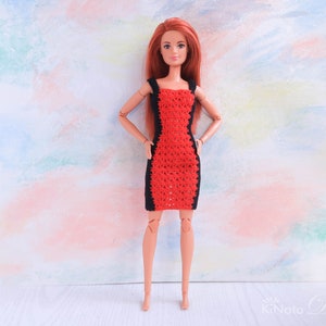May include: A red and black crocheted dress for a doll. The dress has a fitted bodice and a flared skirt. The doll has long red hair and is wearing the dress on a white background.