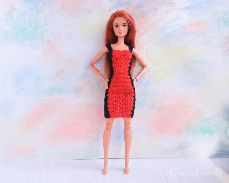 May include: A red and black crocheted dress for a doll. The dress has a fitted bodice and a flared skirt. The doll has long red hair and is wearing the dress on a white background.